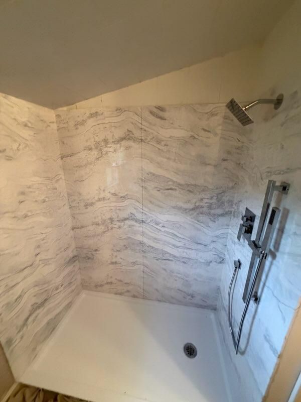Corner view of marble-pattern shower walls and dark fixtures